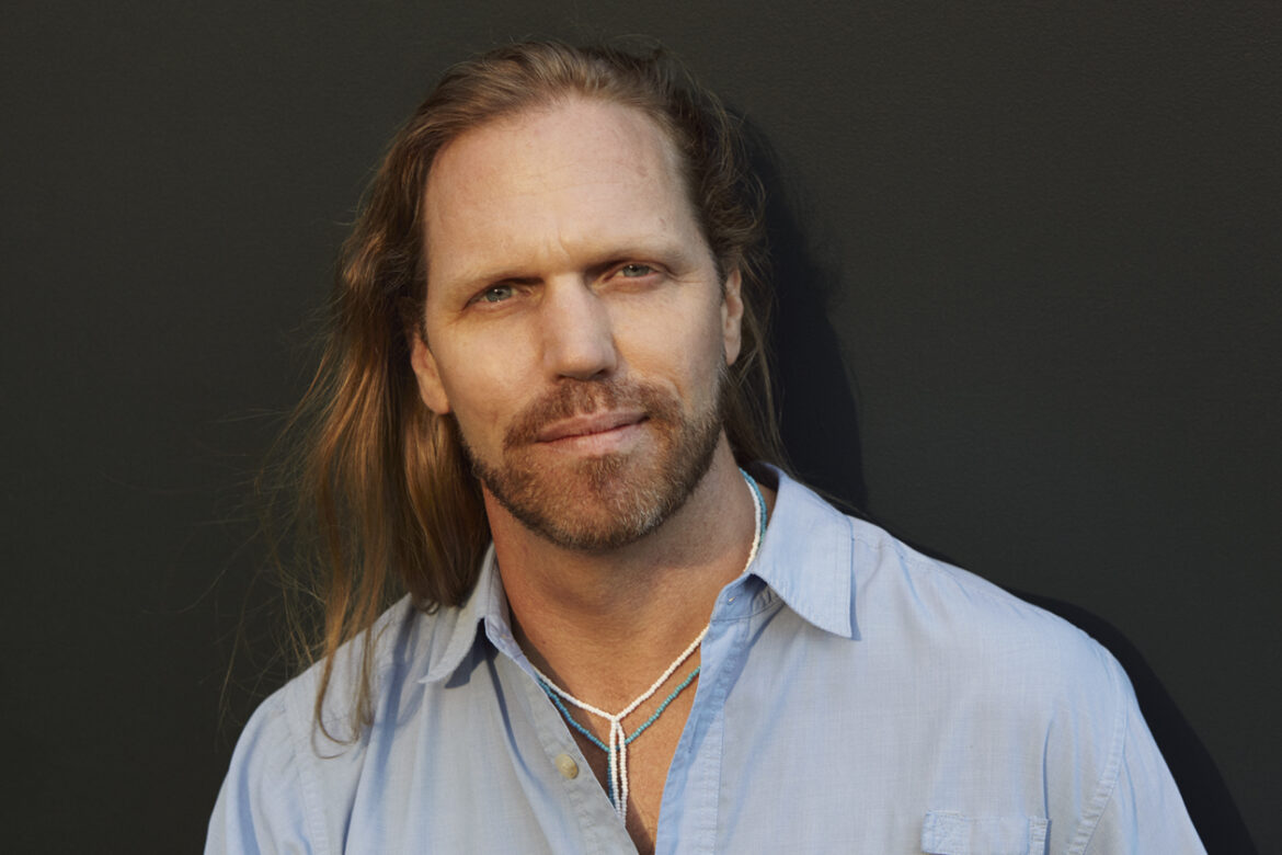 John Lockley with long hair in a blue button-up shirt