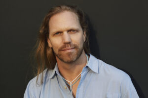 John Lockley with long hair in a blue button-up shirt