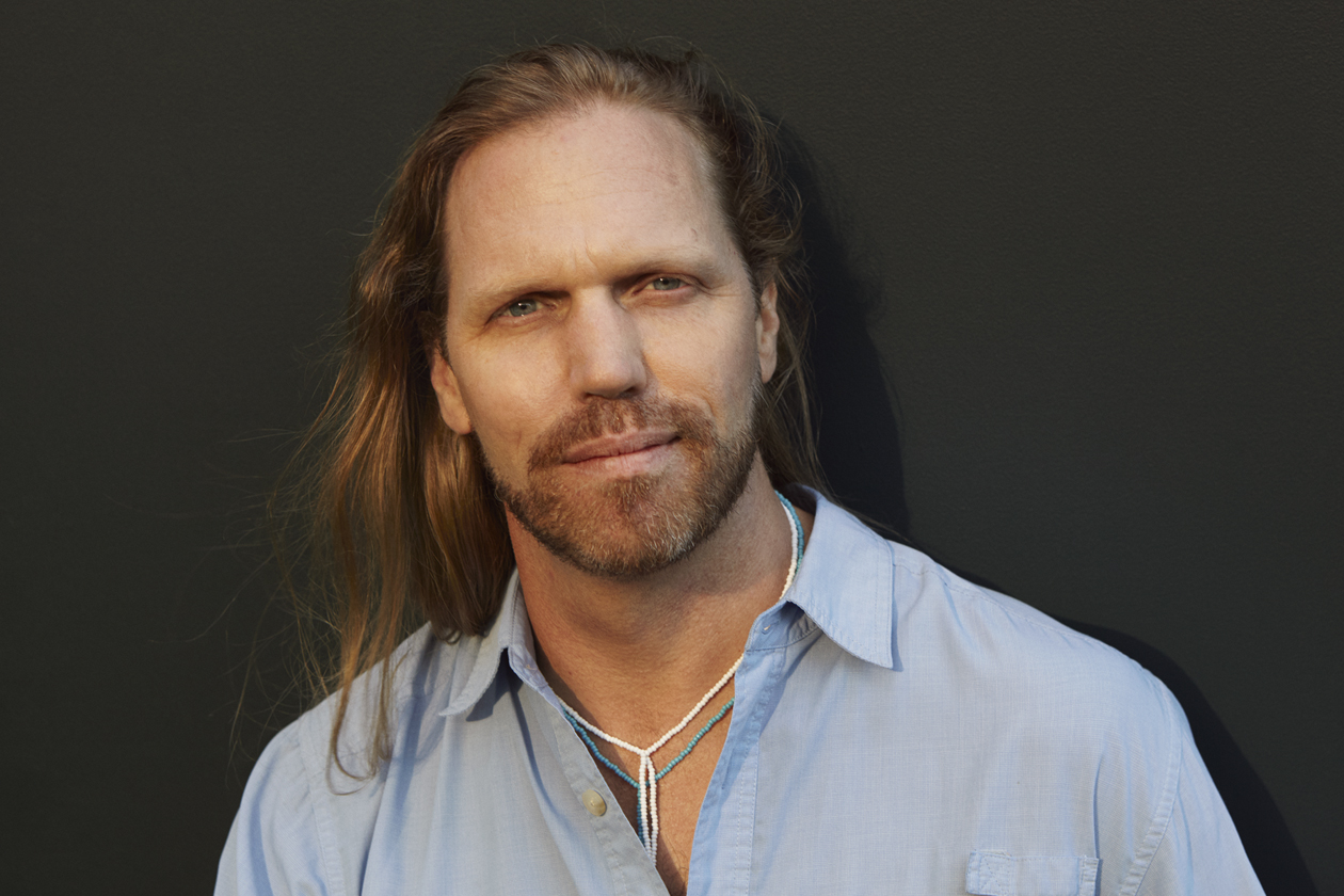 John Lockley with long hair in a blue button-up shirt